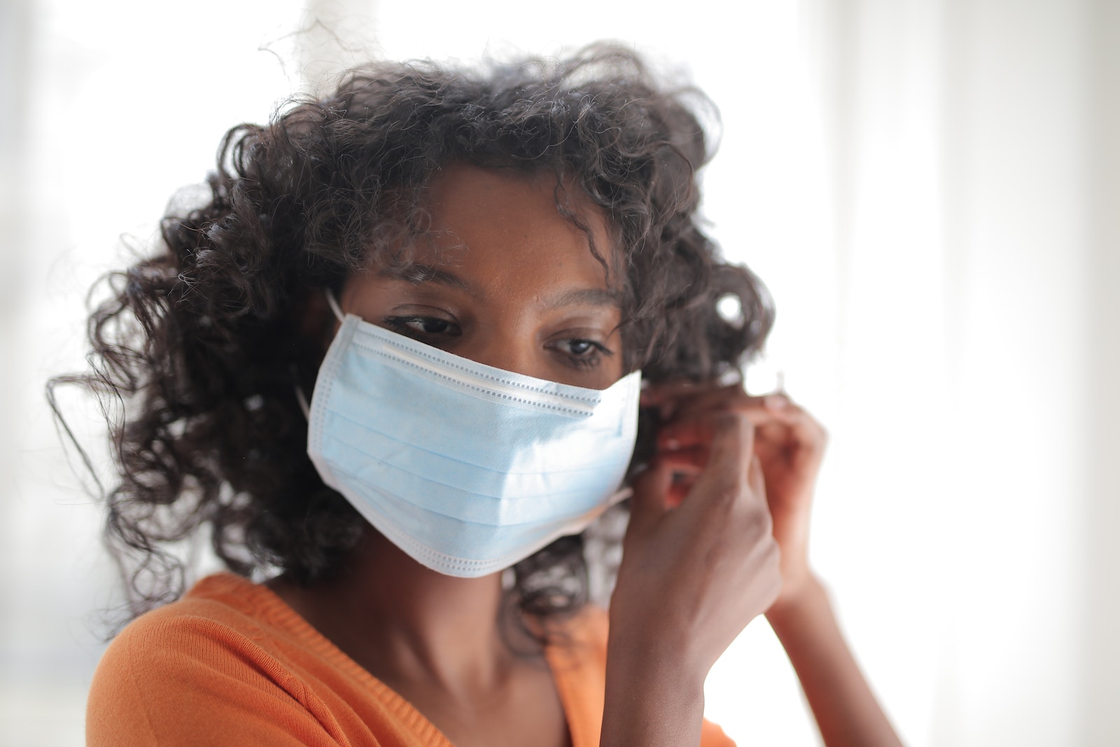 Concentrated curly haired African American woman in casual outfit wearing medical mask and looking down